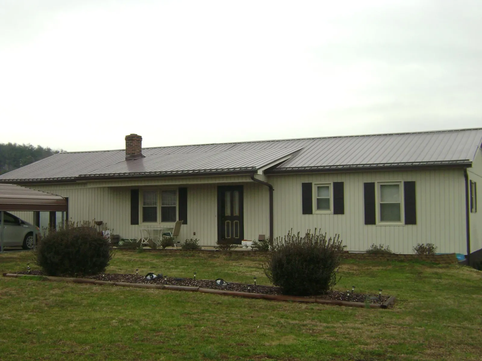 Brown metal roof on a cream sided ranch home with a brick chimney in Winter Park